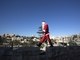 Em Jerusalém, um palestino vestido de Papai Noel passeia pelo muro da antiga cidade com o saco do bom velhinho e um pinheiro de Natal 