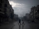 Pai e filho voltam para casa enquanto, ao fundo, surge uma fumaça provocada pela artilharia das forças pró-governo na cidade de Aleppo, na Síria 