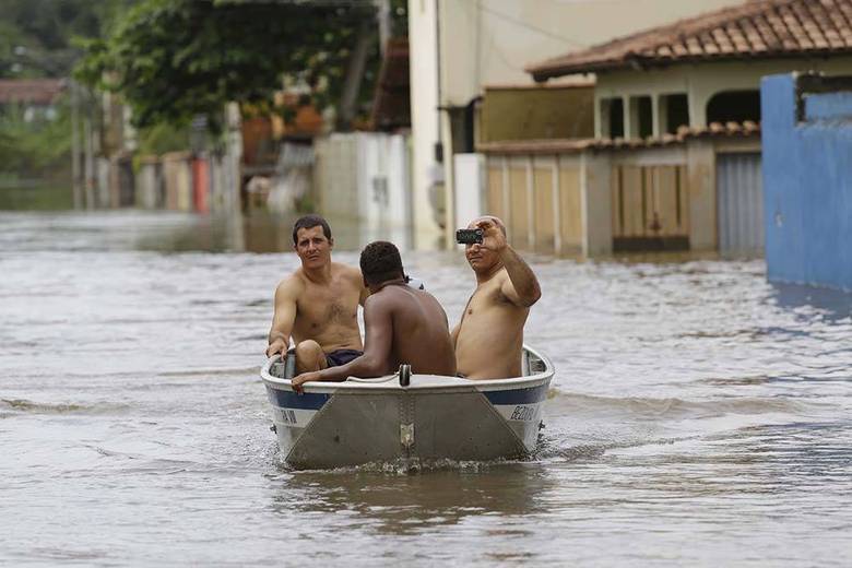 O Espírito Santo já registrou 21 mortes em decorrência das chuvas. Os temporais também provocaram a morte de 17 pessoas em Minas Gerais. Na foto, residentes da comunidade de Jacaraípe usam barco para percorrer rua alagada no município de Serra, cerca de 25 km ao norte de Vitória (ES)