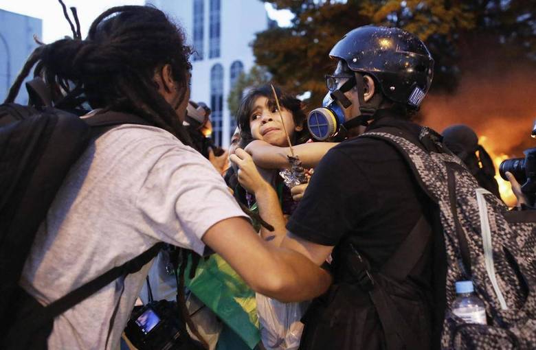 Fotógrafos ajudam a menina após o carro pegar fogo. Os protestos reuniram mais de 2.000 manifestantes em São Paulo. Uma das maiores críticas era sobre o uso do dinheiro público para a realização do campeonato mundial de futebol