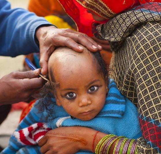 Uma criança teve seu cabelo cortado para celebrar o festival Kumbh Mela