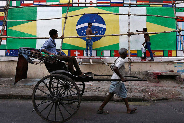 Um puxador de riquixá passa na frente de uma parede decorada com bandeiras do Brasil, em Kolkata, também na Índia