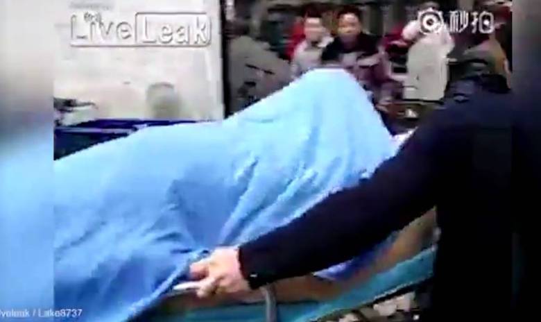 Apesar de estar escondida sob o cobertor, a suposta mulher
parece estar se movendo. Ao redor da maca, uma multidão de pessoas assiste
ao transporte do corpo