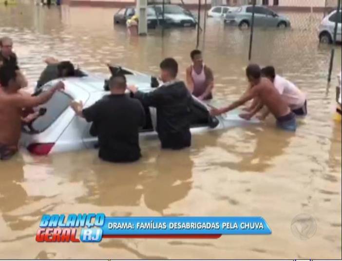 Moradores tentam remover um carro submerso pelas águas do temporal