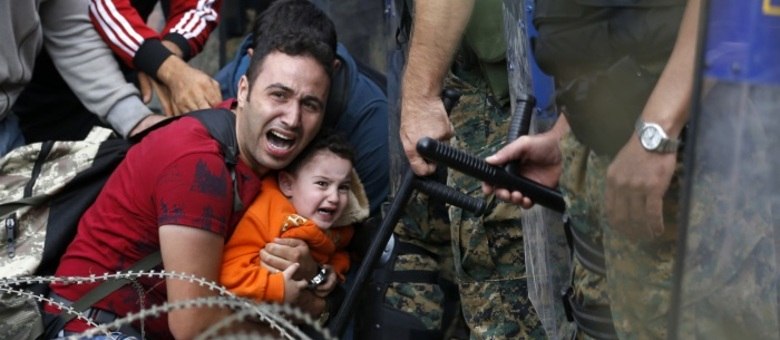  Um migrante, protegendo seu filho pequeno, recua durante motim entre refugiados e policiais macedônios perto da estação ferroviária da cidade fronteiriça de Idomeni, ao norte da Grécia
