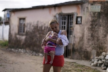 Gleyse da Silva segura a filha com microcefalia diante de sua casa, em Recife
