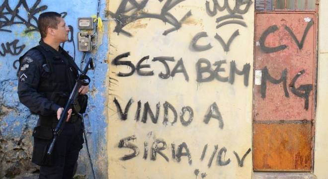 Policial militar em operação na Mangueira; inscrição em muro compara favela à Síria