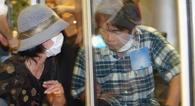Homem e mulher separados por um vidro no aeroporto de Hanoi depois de voltar da China durante a epidemia de Sars