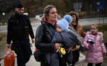 Grande parte das mães, porém, conseguiu retirar os filhos da guerra. Nesta imagem, um policial de fronteira da Polônia (à esquerda) ajuda uma mulher a carregar a bagagem de refugiada enquanto ela segura um bebê nos braços. A foto mostra outras crianças na mesma situação dos refugiados