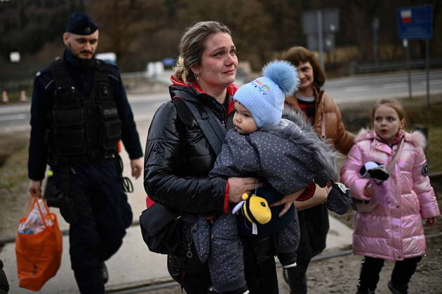 Grande parte das mães, porém, conseguiu retirar os filhos da guerra. Nesta imagem, um policial de fronteira da Polônia (à esquerda) ajuda uma mulher a carregar a bagagem de refugiada enquanto ela segura um bebê nos braços. A foto mostra outras crianças na mesma situação dos refugiados