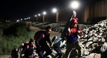  Imigrantes em busca de asilo nos Estados Unidos caminham ao longo da cerca da fronteira, nesta quinta-feira (11)