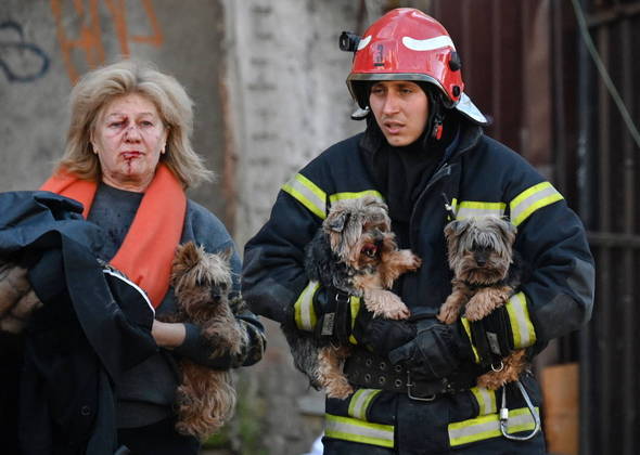 Bombeiro ajuda mulher ferida a carregar os cães depois dos múltiplos ataques a Kiev e outras cidades ucranianas