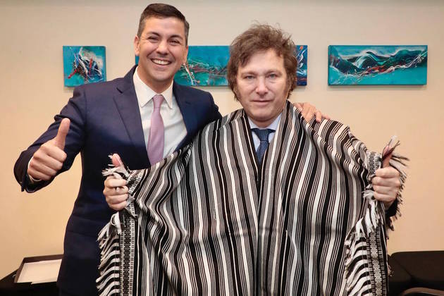 This handout picture released by the Paraguayan Presidency shows Paraguay's President Santiago Peña (L) posing next to Argentina's President-elect Javier Milei after giving him a "Poncho Para'i de 60 Listas" as a present during a bilateral meeting in Buenos Aires on December 9, 2023, on the eve of the swear-in ceremony. The "Poncho Para’i de 60 Listas" is a handmade garment from Paraguay consisting of three parts: the body, the fringes, and the fajita, or guard, and is part of UNESCO's intangible cultural heritage.
