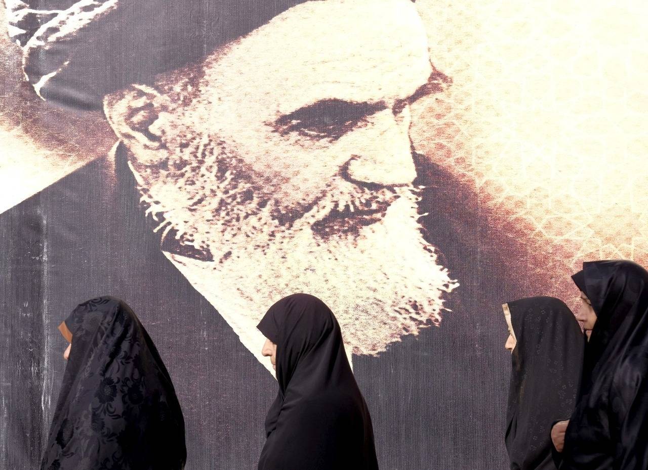 Mulheres iranianas passam por um pôster do falecido líder do Irã, aiatolá Ruhollah Khomeini