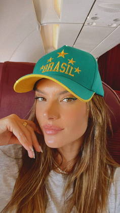 A modelo Alessandra Ambrosio posou dentro de um avião, exibindo um boné do Brasil, em tons verdes e amarelos