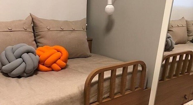 Almofada do tipo nó em tom laranja e cinza decoram o quarto