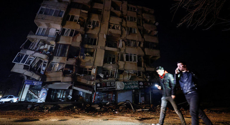 Pessoas passam em frente a prédio destruído após o terremoto em Hatay, na Turquia