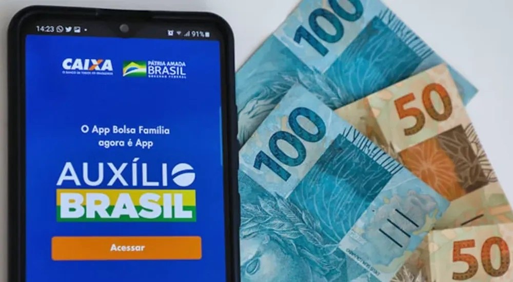 Aplicativo do Auxílio Brasil no celular, ao lado de notas de reais. Estadão Conteúdo / André Melo Andrade / Immagini