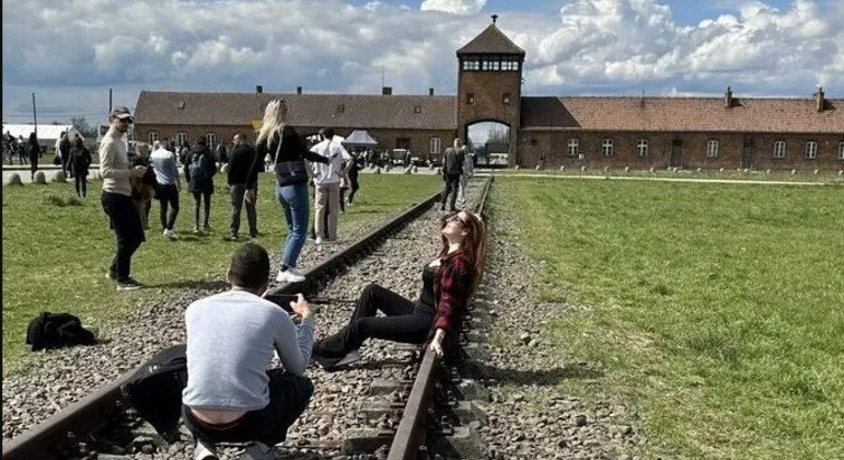 Turista faz pose desrespeitosa em frente ao antigo campo de concentração de Auschwitz