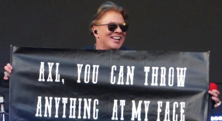 Axl Rose segura um cartaz que brinca com o assunto do microfone