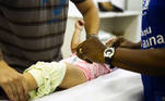 Profissional de saúde vacina bebê enquanto o pai segura suas pernas