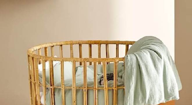 Berço de vime com formato arredondado. e tapete felpudo