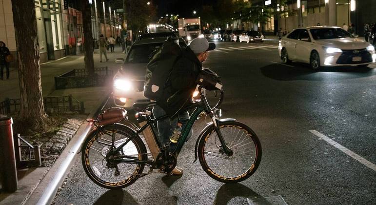 Edgar Sapon, andando de bicicleta elétrica, observa o tráfego antes de pegar um pedido de delivery