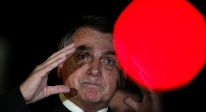 Bolsonaro falando a apoiadores em área externa, à noite, com olhar consternado