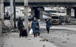 Pessoas carregam seus pertences, nesta sexta (4), em uma avenida, em meio aos escombros, em Kiev, capital da Ucrânia