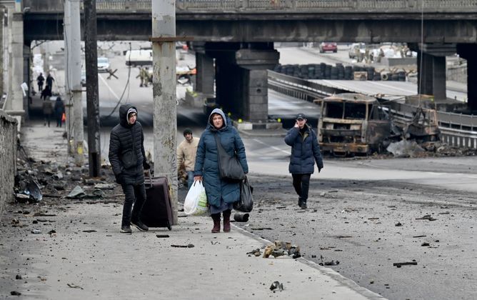 Pessoas carregam seus pertences, nesta sexta (4), em uma avenida, em meio aos escombros, em Kiev, capital da Ucrânia