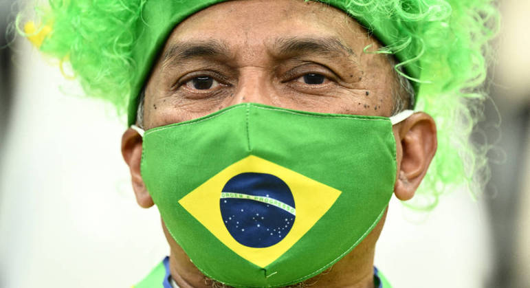 Torcedor usa uma máscara com a bandeira brasileira e se protege da Covid enquanto apoia a seleção no Catar