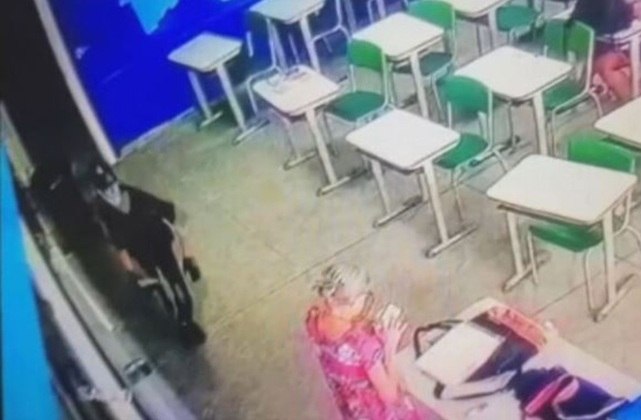 Câmeras de segurança da escola gravaram os momentos do ataque.Na imagem, a professora Elizabeth Tenreiro, de 71 anos,  está junto à mesa, na sala da oitava série, olhando o celular.