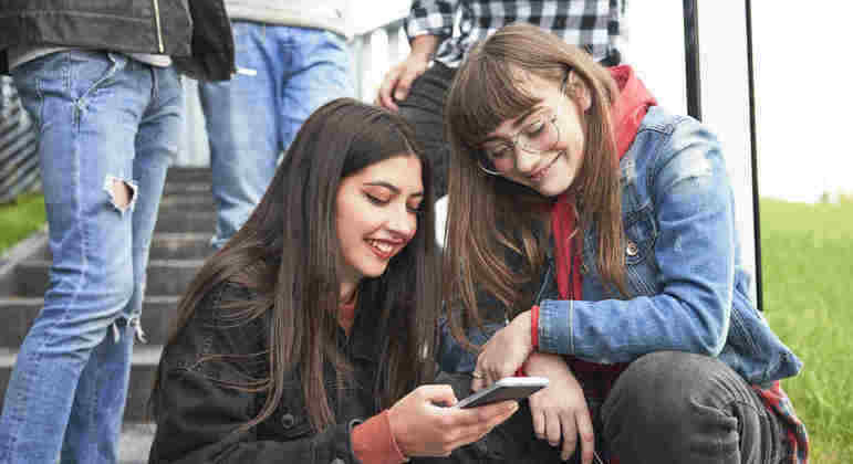 Dois adolescentes, menino e menina, jogam jogo para celular em smartphones