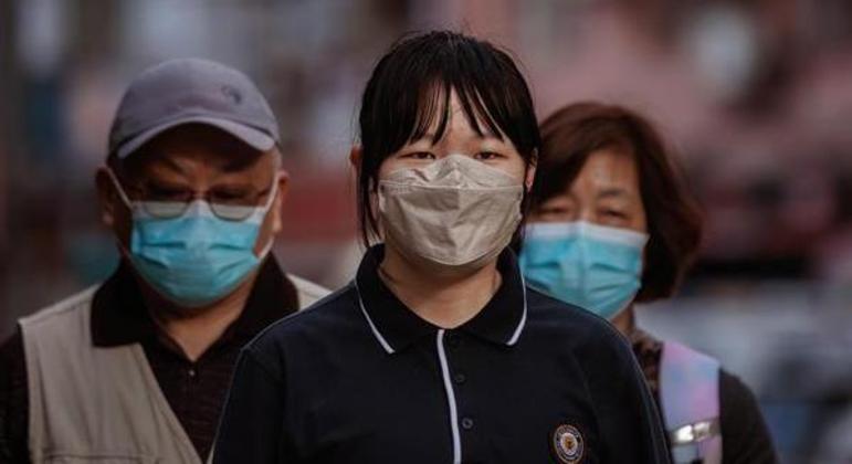 Pessoas usando máscaras caminham do lado de fora de um hospital em Xangai, na China