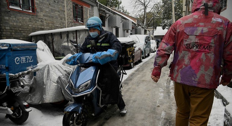 Entregador de comida atravessa uma viela em dia de neve em Pequim