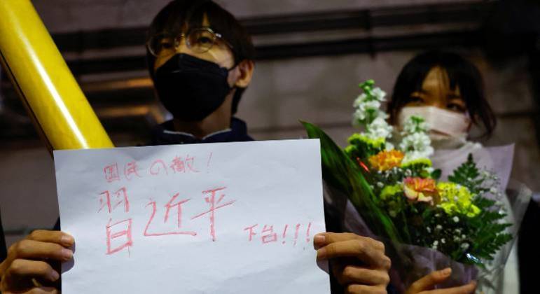 Homem segura folha com a frase 'renúncia de Xi Jinping' durante protesto