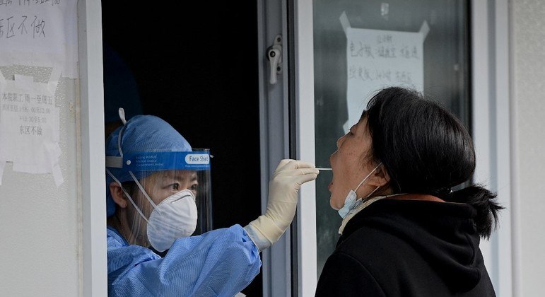 Um trabalhador da saúde pega uma amostra com um cotonete de uma mulher para ser testada para o coronavírus, em Pequim