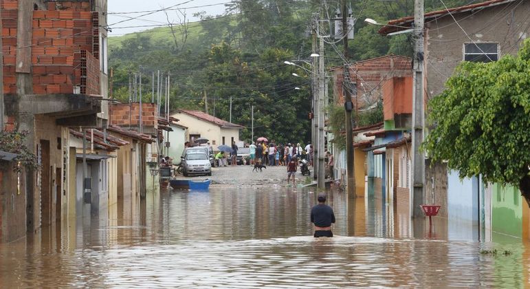 Homem com água praticamente na cintura em rua alagada após chuvas em Minas Gerais