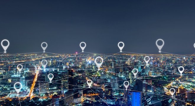 Cidade com vários prédios iluminados durante a noite e símbolos de localização ilustrados e sobrepostos