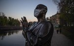 A estátua de Sri Chinmoy usando máscara protetora na margem do rio Vltava ao pôr do sol em Praga, República Tcheca