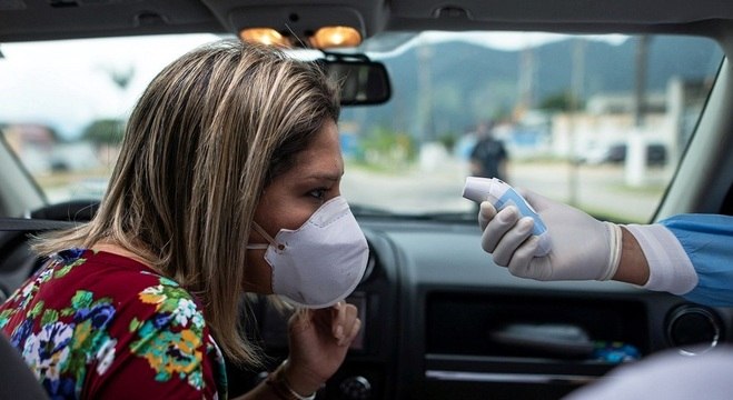 Profissional de saúde tira temperatura de motorista em São Sebastião (SP)