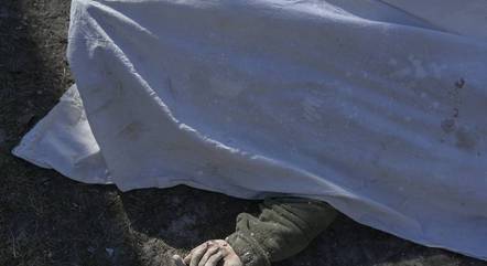 Foto tirada em 19 de março de 2022 mostra o corpo de um soldado ucraniano coberto com um lençol ao lado da escola militar atingida por foguetes russos na sexta-feira (18), em Mykolaiv, sul da Ucrânia