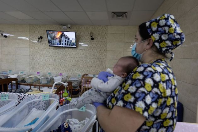 Mulher segura recém-nascido enquanto vê na TV imagens da guerra