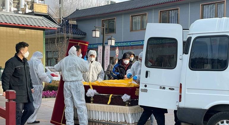 Trabalhadores em trajes de proteção transferem um corpo em um caixão em uma funerária
