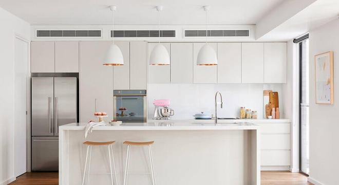 Cozinha com ilha toda branca decorada com pendentes