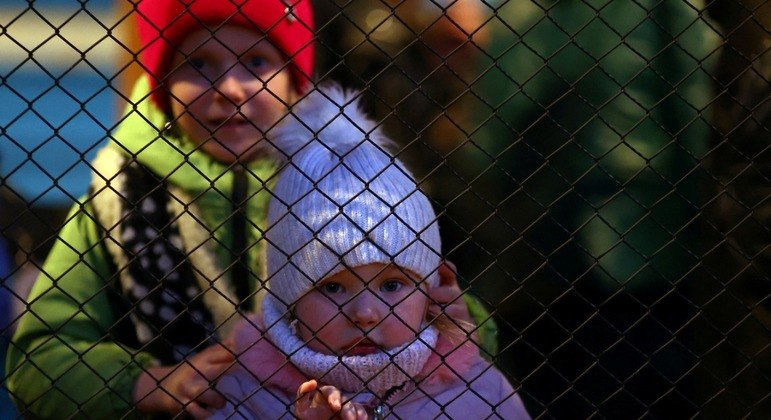 Menina ucraniana olha através de uma cerca ao chegar a uma estação de trem na Polônia