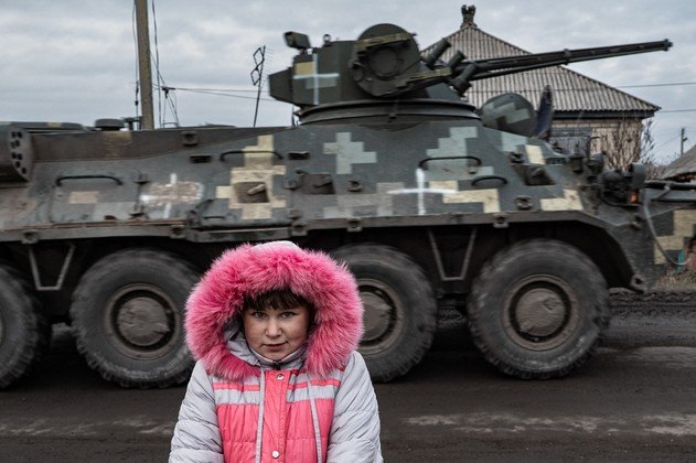 À beira da estrada e cercada por ruínas, Lisa Shtanko acompanha a passagem dos soldados ucranianos, que sempre têm um presente para as crianças que, como ela, vivem em meio ao caos da guerra. Vestida com um casaco rosa-neon, ela tem um tom de voz alegre, mas que não esconde o medo