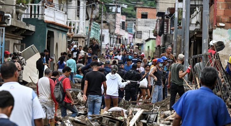 Pessoas caminham entre os escombros causados pelas chuvas