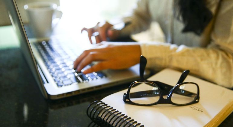 Pessoa trabalhando no computador com óculos ao lado 