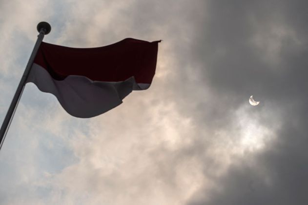 O eclipse solar acontece quando a lua  fica entre o sol e a Terra, o que faz surgir uma sombra sobre  o nosso planeta. Na foto, a bandeira da Indonésia e o eclipse ao fundo